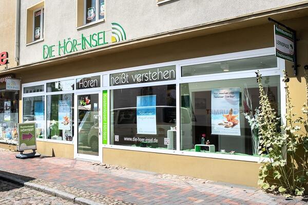 Fassade eines Hörakustik-Fachgeschäfts mit großem Schaufenster und Werbeplakaten.