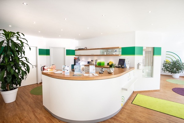 Heller Empfangsbereich einer modernen Arztpraxis mit Pflanzen, Tresen und Informationsmaterial.