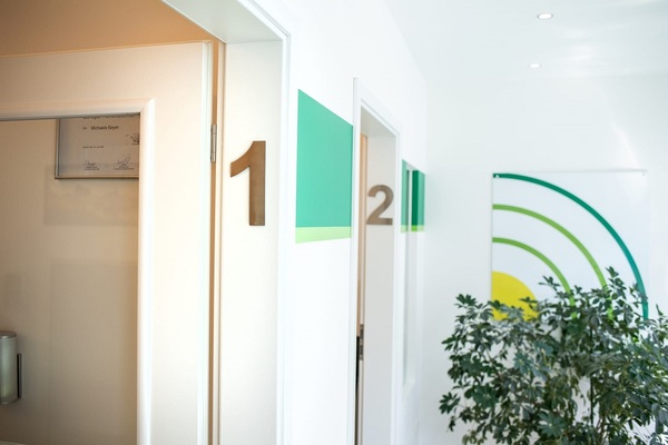 Helles Wartezimmer in einer Arztpraxis mit Türen zu Behandlungsräumen und moderner Deko.